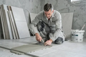 Carreleur professionnel appliquant de la colle à carrelage sur un sol en béton avec une spatule crantée dans une salle de bain en rénovation