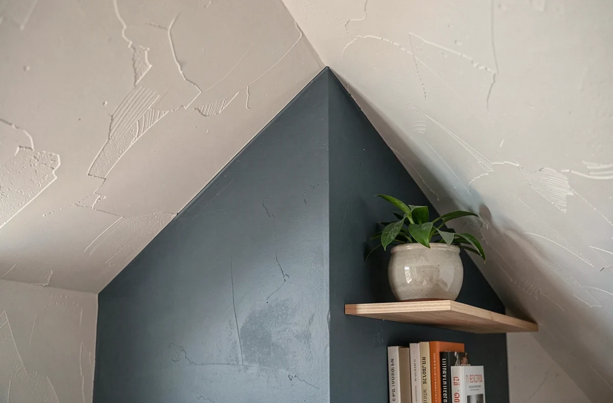 Détail d'une chambre mansardée avec mur bas peint en bleu foncé pour accentuer la hauteur sous plafond