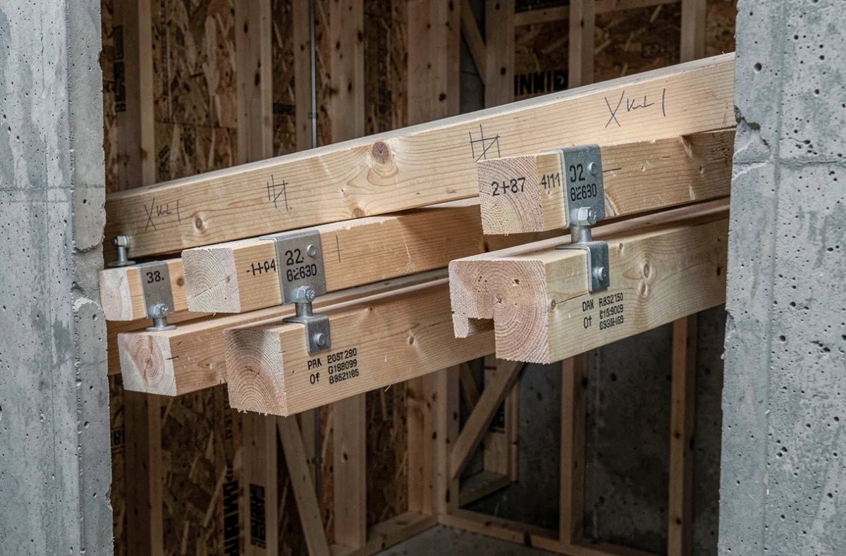 Détail des sections de solives bois avec sabots métalliques et marquages dimensionnels sur chantier