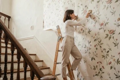 Femme posant du papier peint fleuri sur le mur d'un escalier haussmannien avec une brosse à encoller